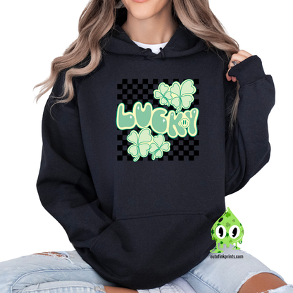 A person wearing a black hoodie with a checkered pattern and a graphic that includes the text 'LUCKY' and clover designs in green.