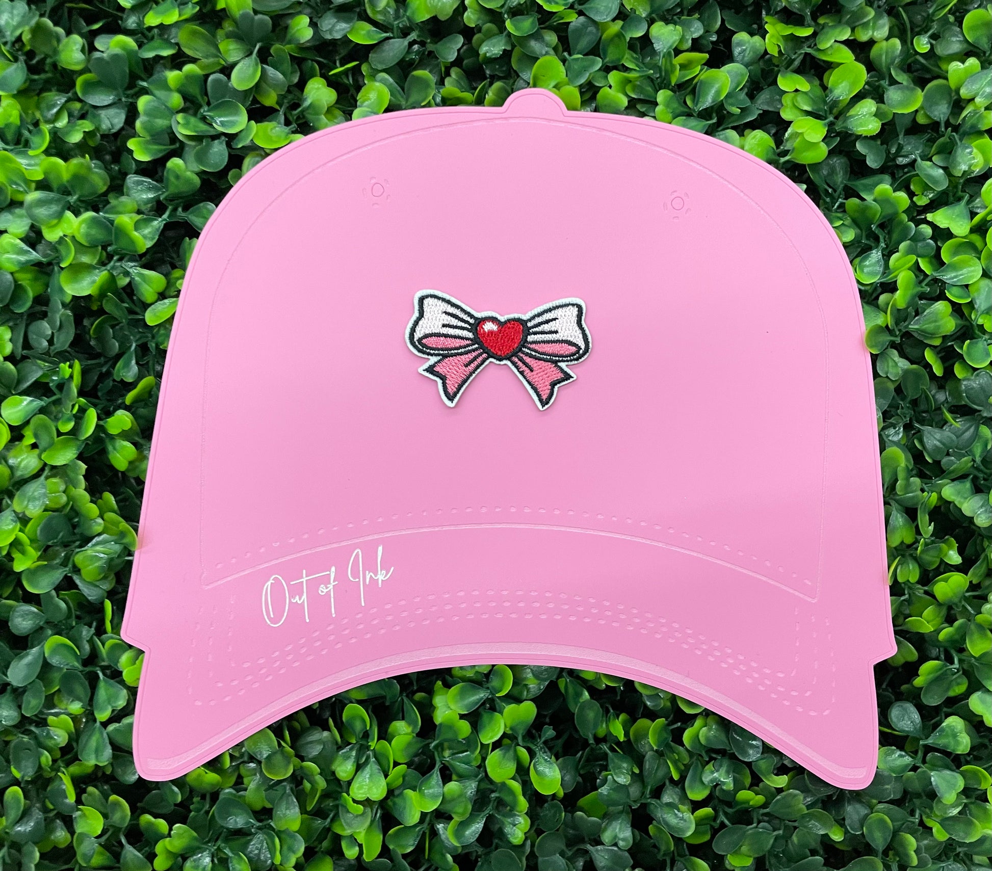 A pink hat that has a patch with a pink and white bowtie design and a heart in the center