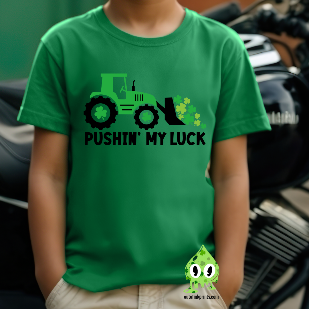 Child wearing a green t-shirt with the text 'PUSHIN' MY LUCK' and a graphic of a tractor and clover.