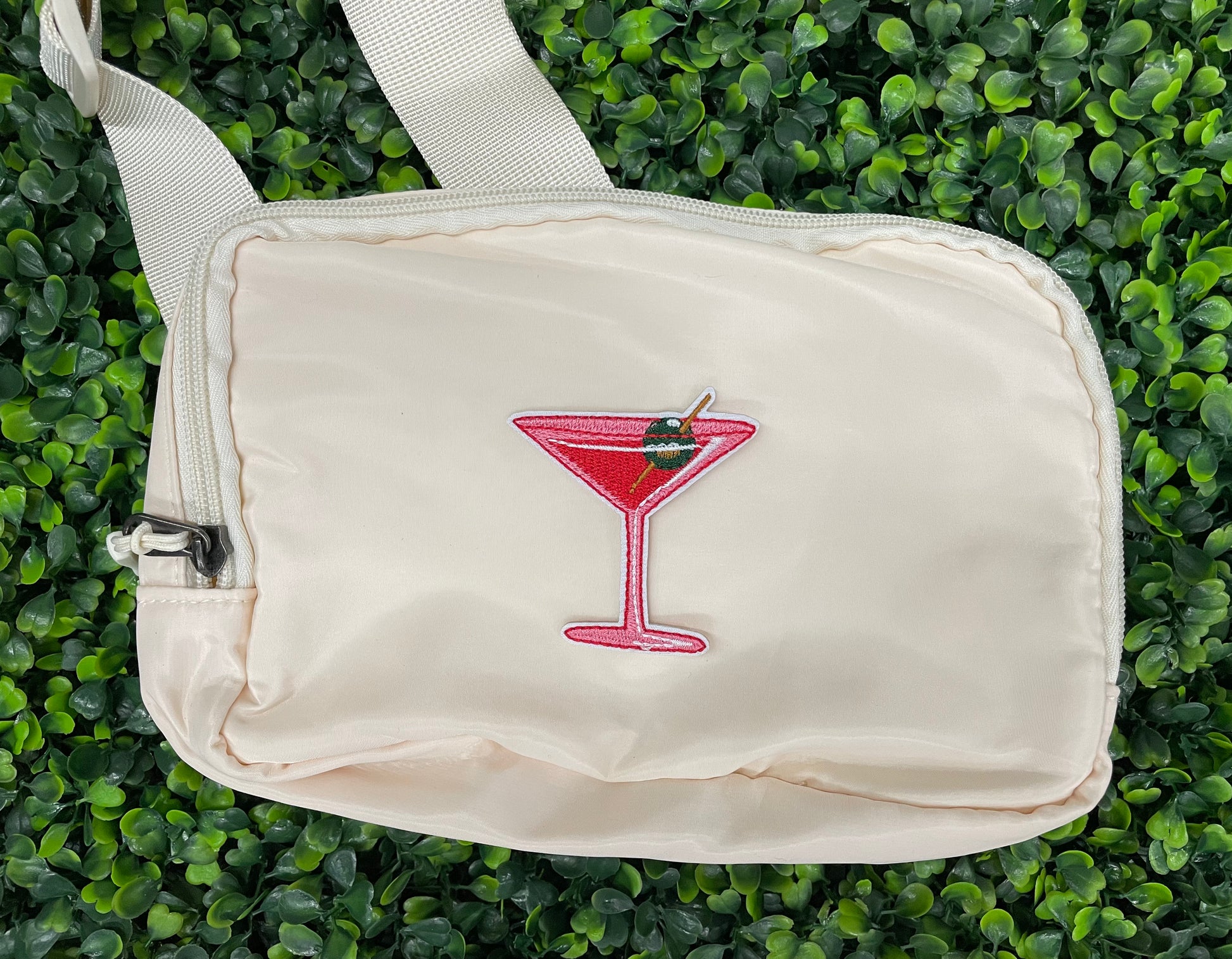 An iron-on patch depicting a red martini glass with a green olive, held onto a white shoulder bag
