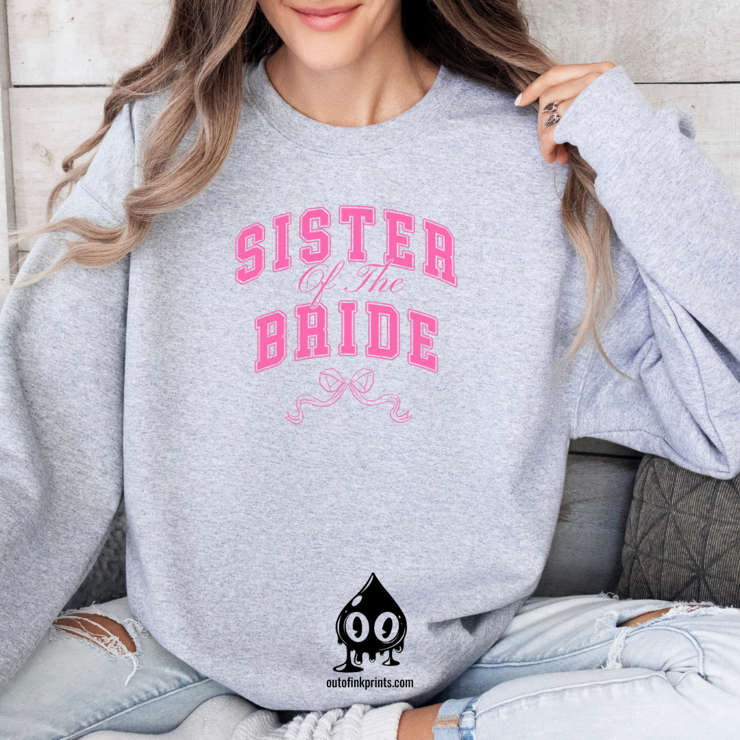 A woman wearing a gray sweatshirt with 'Sister of the Groom' text and a pink bow design on it.