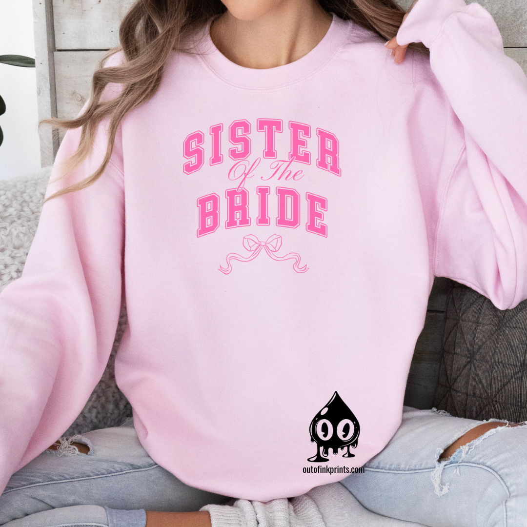 A woman wearing a pink sweatshirt with 'Sister of the Groom' text and a pink bow design on it.