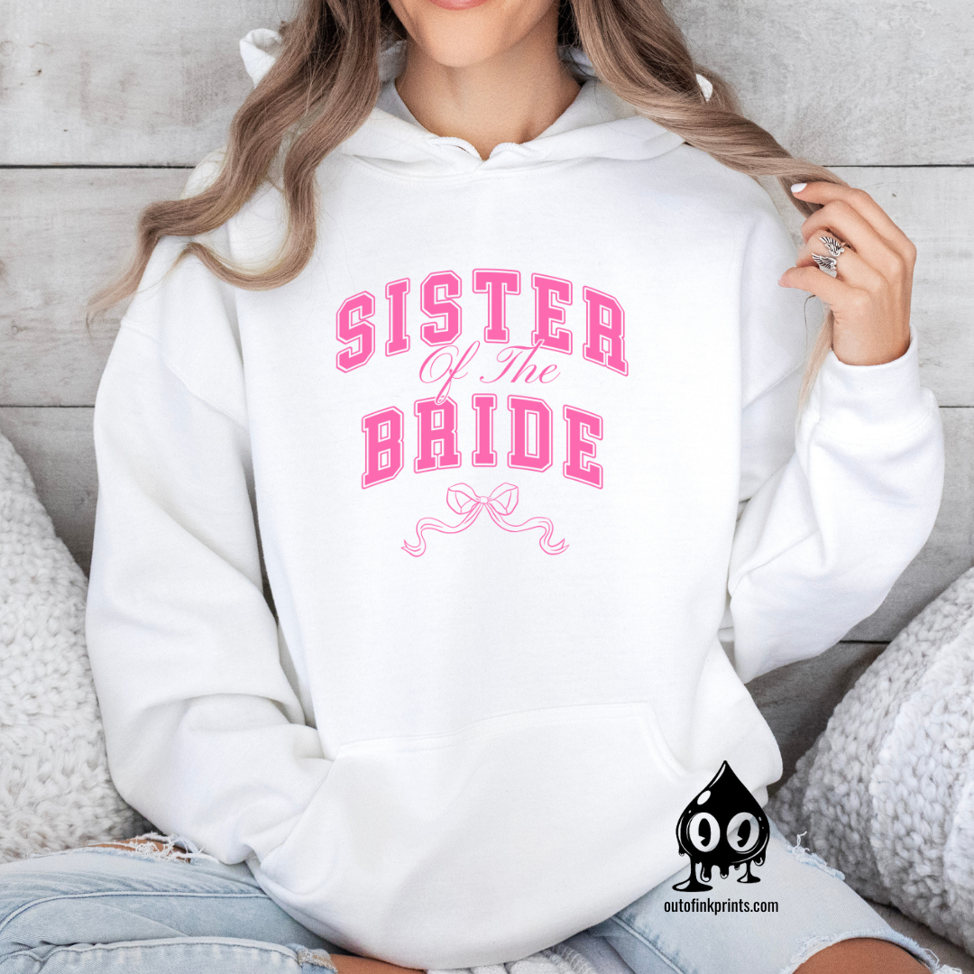 A woman wearing a white hoodie with 'Sister of the Bride' text and a pink bow design.