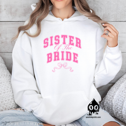 A woman wearing a white hoodie with 'Sister of the Bride' text and a pink bow design.