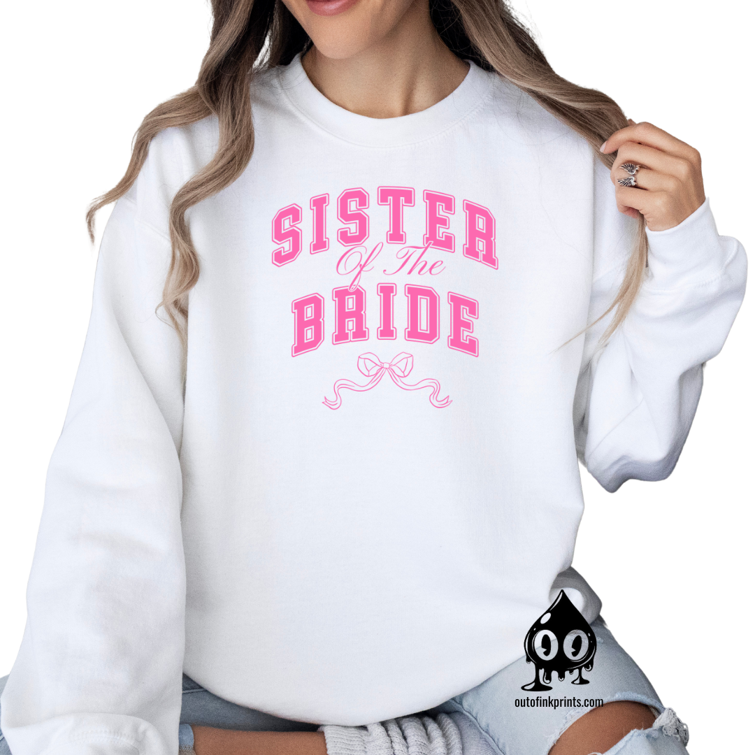 A woman wearing a white sweatshirt with 'Sister of the Groom' text and a pink bow design on it.