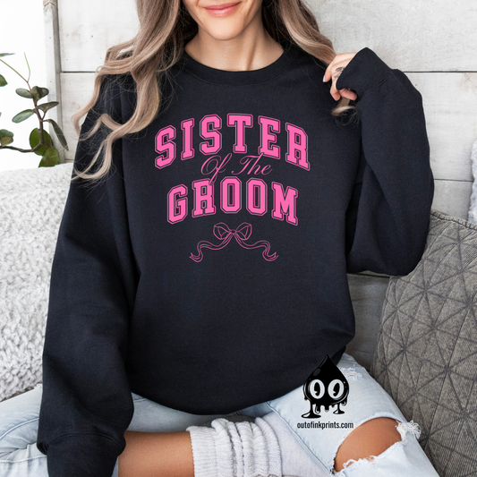 A woman smiling and wearing a black sweatshirt with 'Sister of the Groom' text and a pink bow design on it.