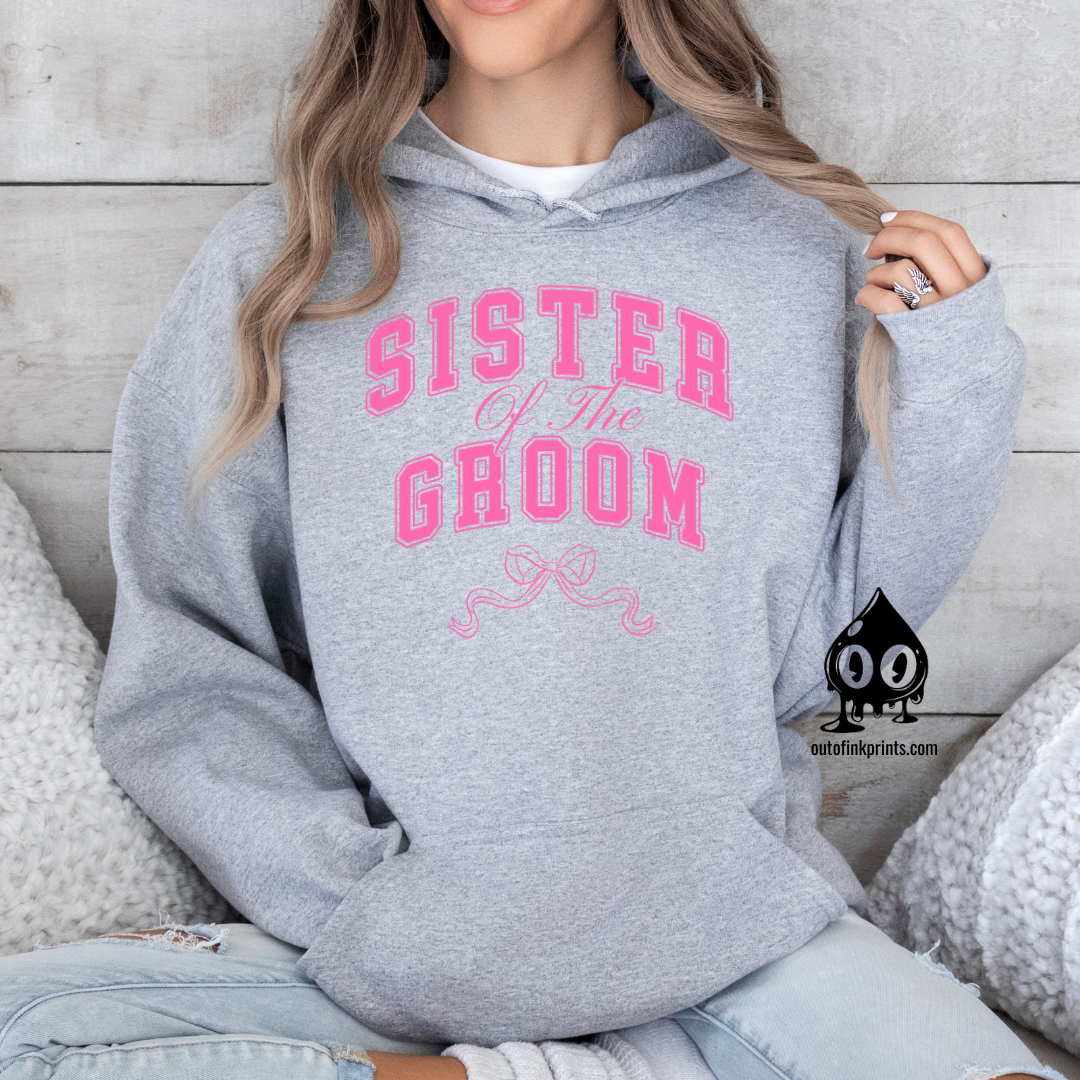 A woman wearing a gray hoodie with 'Sister of the Groom' text and a pink bow design.