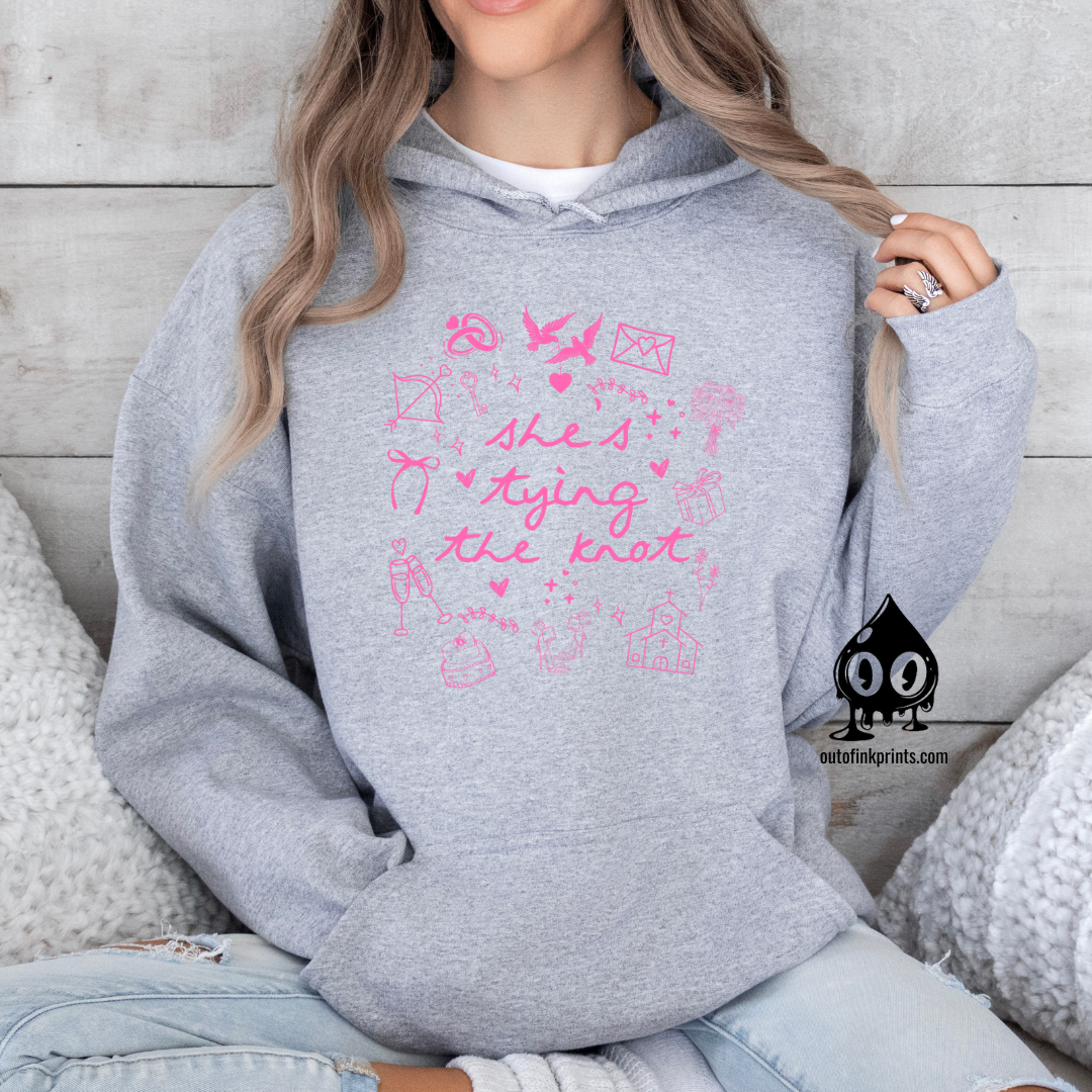 A woman wearing a gray hoodie with pink text and graphics related to bridal themes, such as hearts and bows.