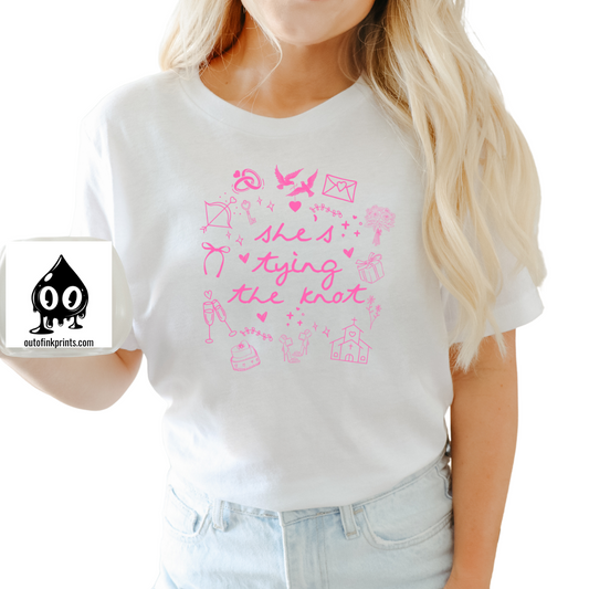 Front view of a white T-shirt with pink text and graphics related to weddings, brides, and bow ties.