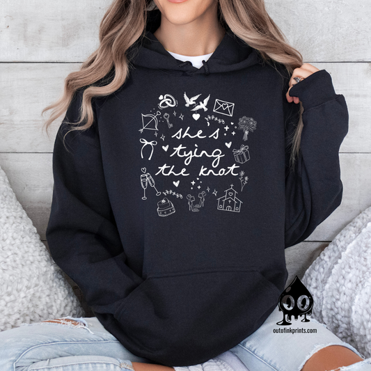 A woman wearing a black hoodie with white text and graphics related to a bride tying the knot.