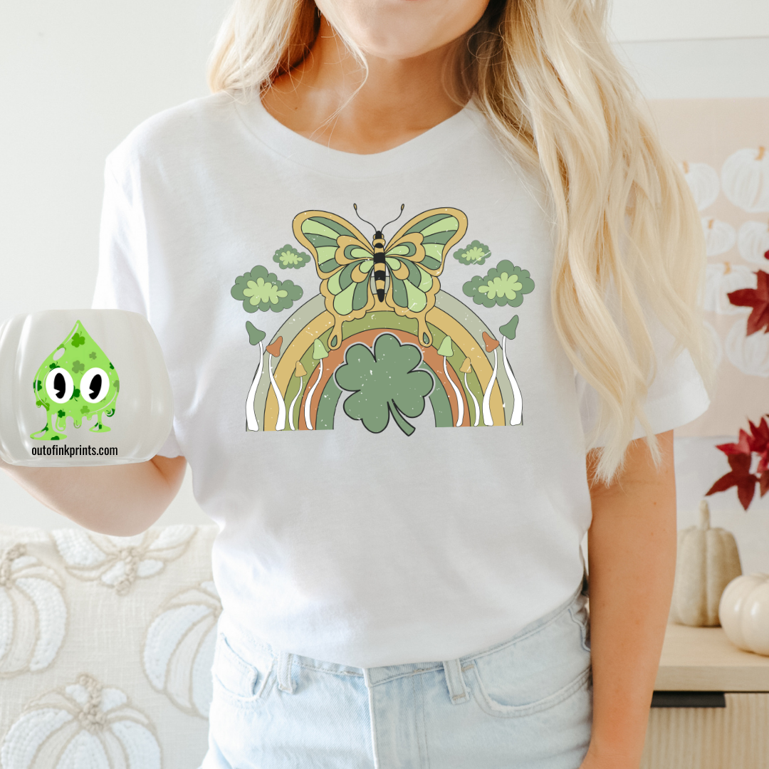 Front view of a white t-shirt with a graphic design of a butterfly and rainbows, predominantly in green color, celebrating St. Patrick's Day.