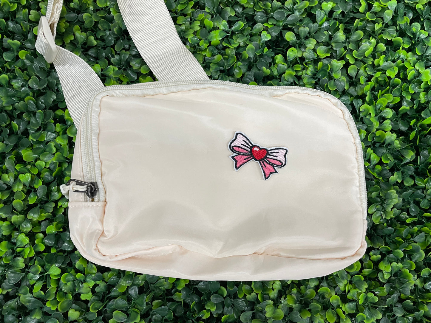 An off-white bag that has a patch with a pink and white bowtie design and a heart in the center