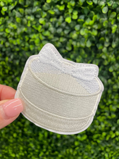 Embroidered patch of a white cake with a white bow placed on top.