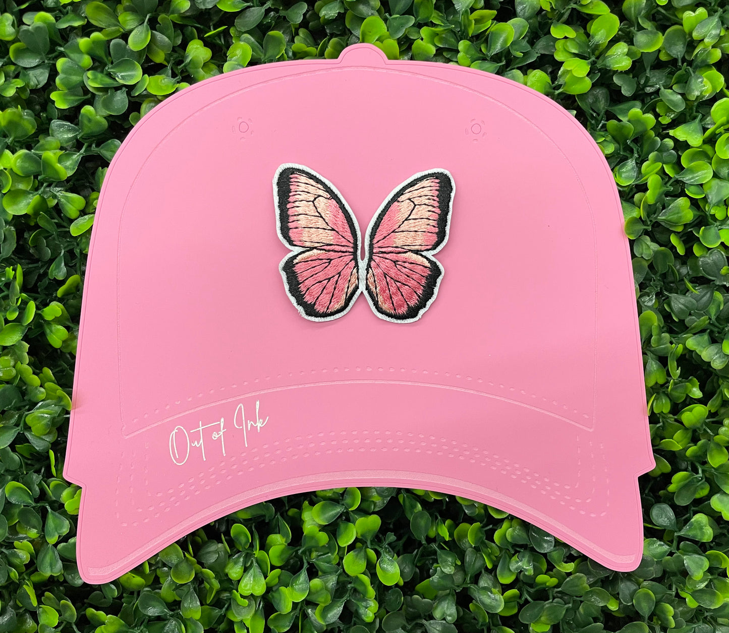 A pink butterfly embroidered patch held onto a pink hat