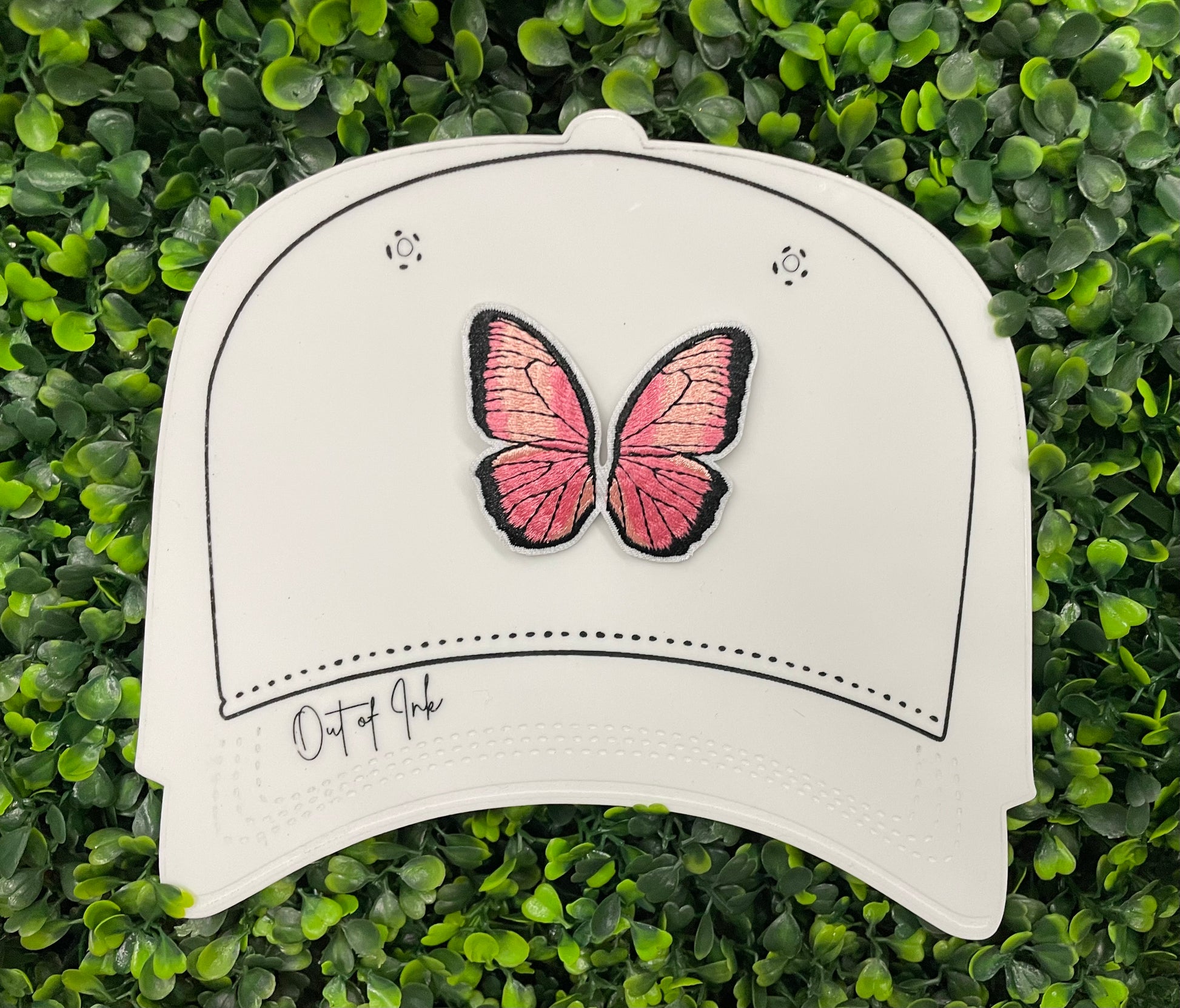 A pink butterfly embroidered patch held against a white hat design
