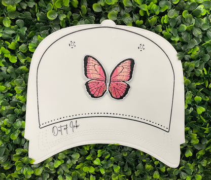 A pink butterfly embroidered patch held against a white hat design