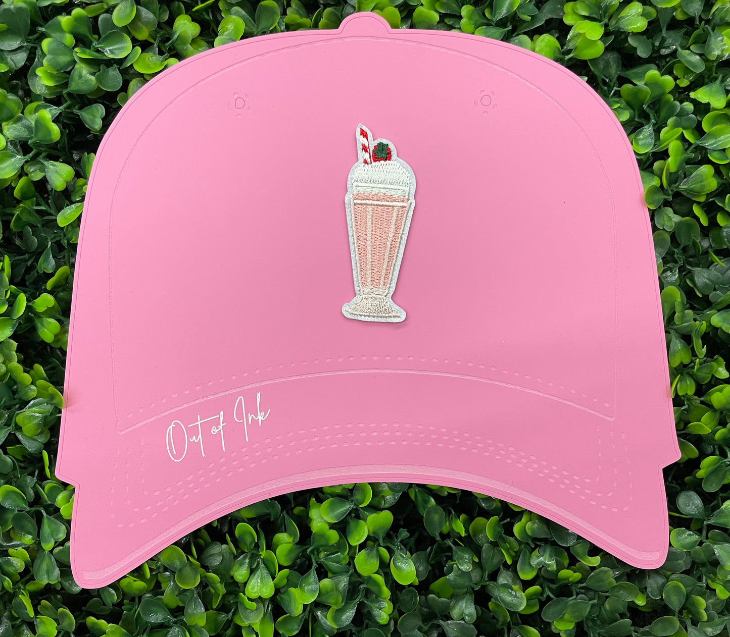 A pink milkshake embroidered patch with a cherry on top, held onto a pink hat