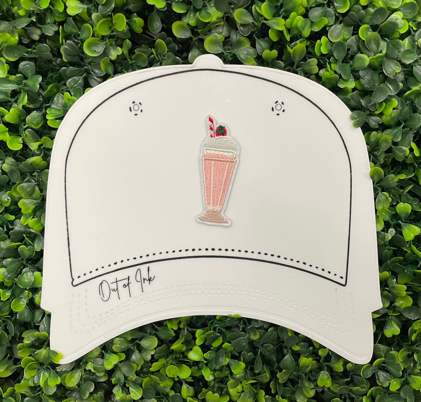 A pink milkshake embroidered patch with a cherry on top, held onto a white hat design 