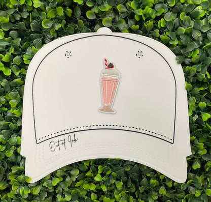 A pink milkshake embroidered patch with a cherry on top, held onto a white hat design 