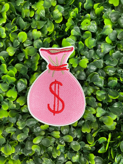 A patch depicting a pink bunched money bag with a red dollar sign
