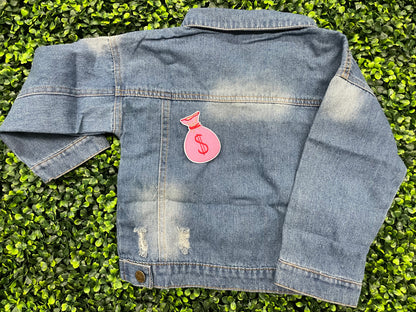 A patch depicting a pink bunched money bag with a red dollar sign, placed on a jean jacket
