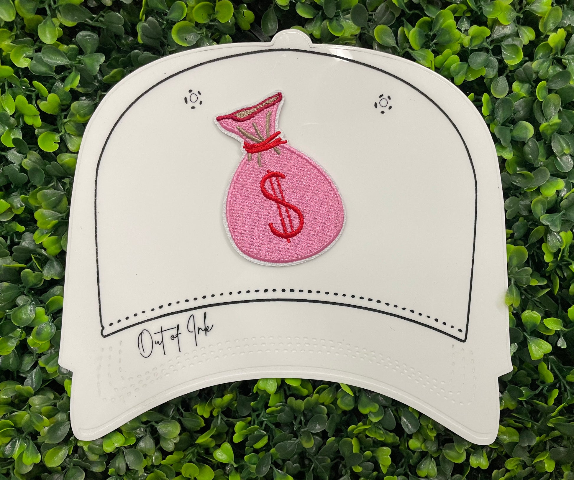 A patch depicting a pink bunched money bag with a red dollar sign, placed on a white hat