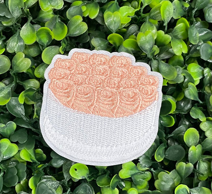 An embroidered patch in the shape of a bundle of roses with pink petals and green leaves, set against a green backdrop