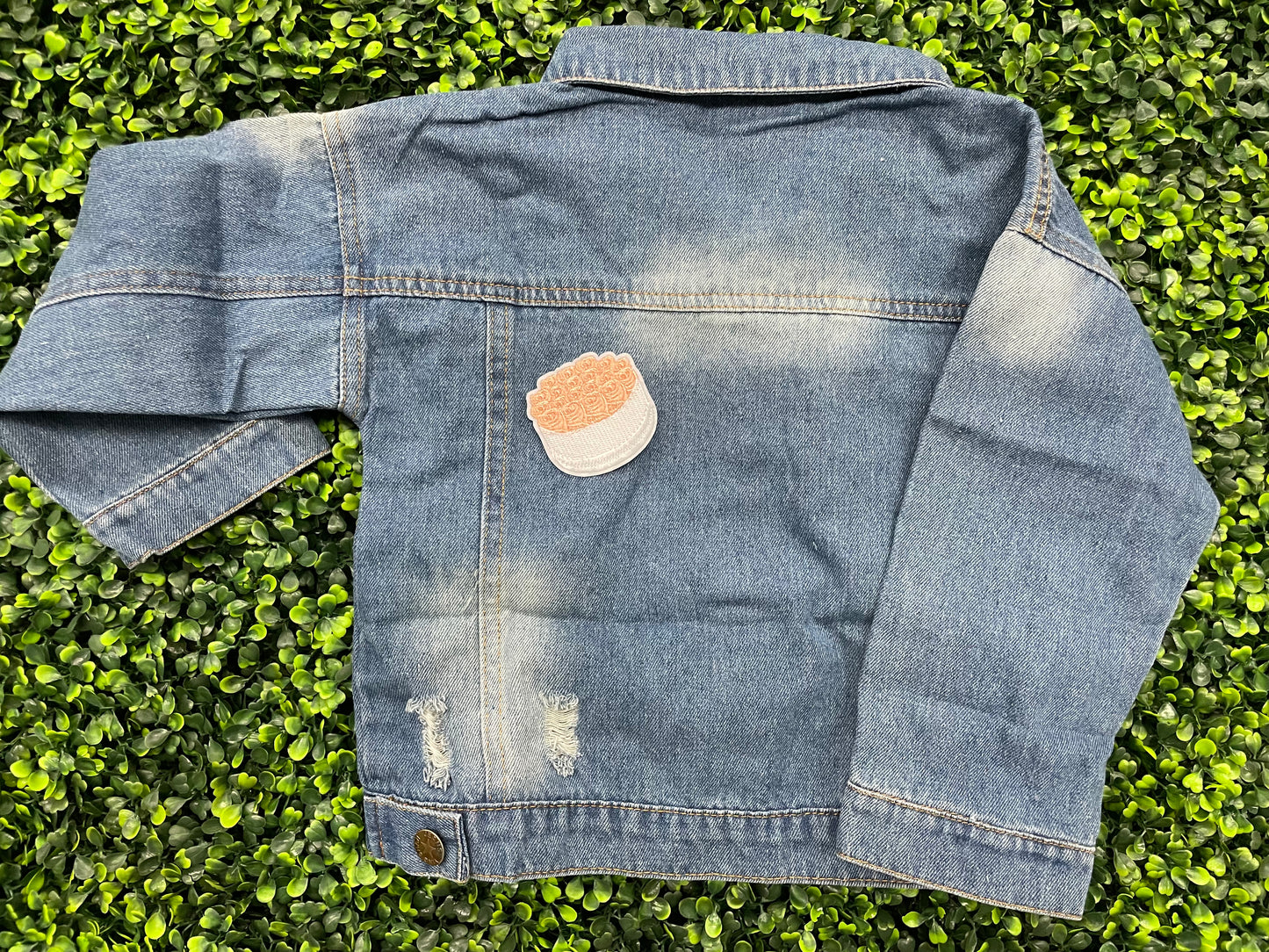 An embroidered patch in the shape of a bundle of roses with pink petals and green leaves, placed on a child's jean jacket