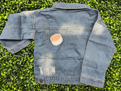 An embroidered patch in the shape of a bundle of roses with pink petals and green leaves, placed on a child's jean jacket