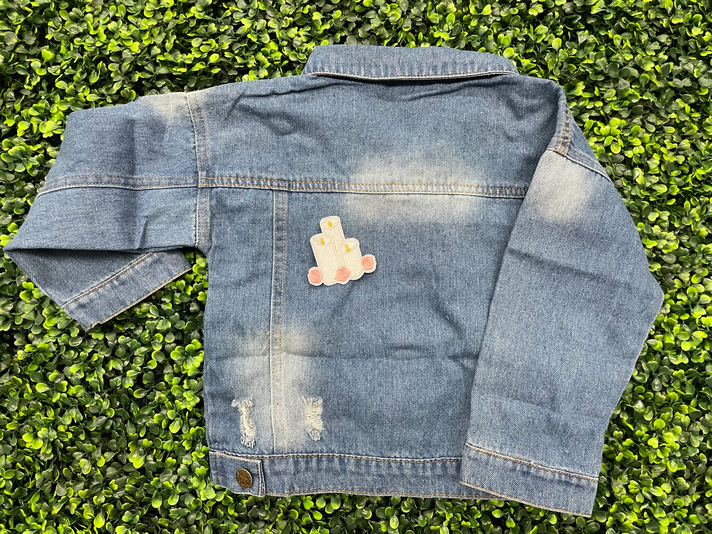 A patch with embroidered candles and roses in pink and yellow colors on a white background, placed on a child's jean jacket