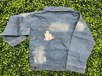 A patch with embroidered candles and roses in pink and yellow colors on a white background, placed on a child's jean jacket