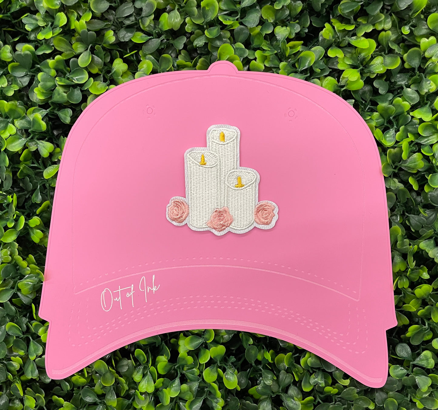 A patch with embroidered candles and roses in pink and yellow colors on a white background, placed on a pink hat