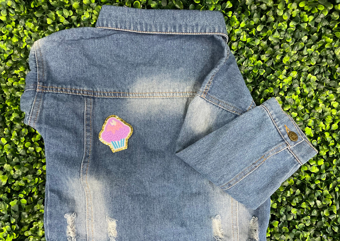 Decorative patch of a cupcake with pink and purple frosting, placed on a children's denim jean jacket 