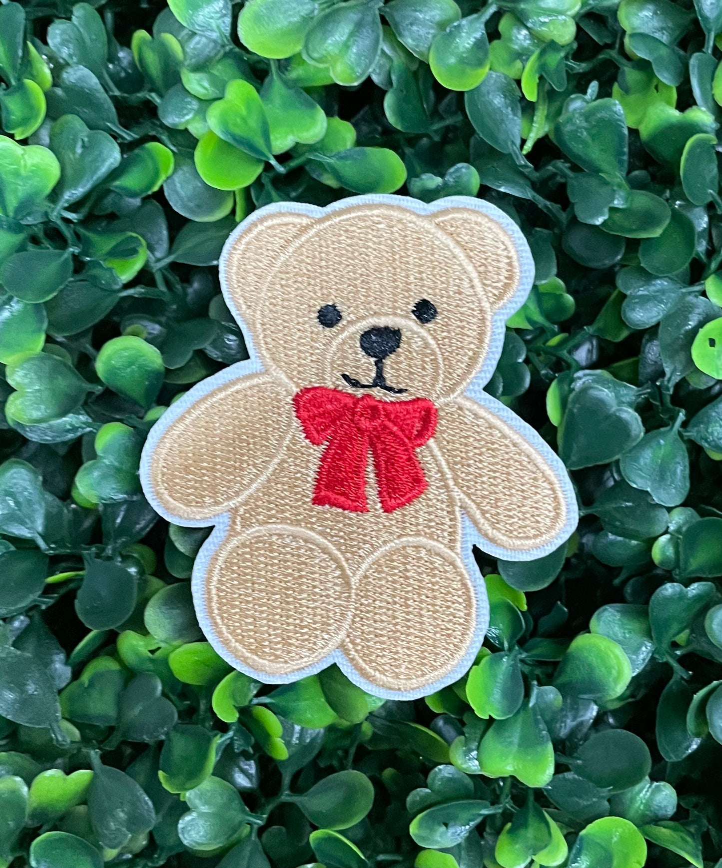 Embroidered Teddy Bear patch with a red bow set on a green backdrop