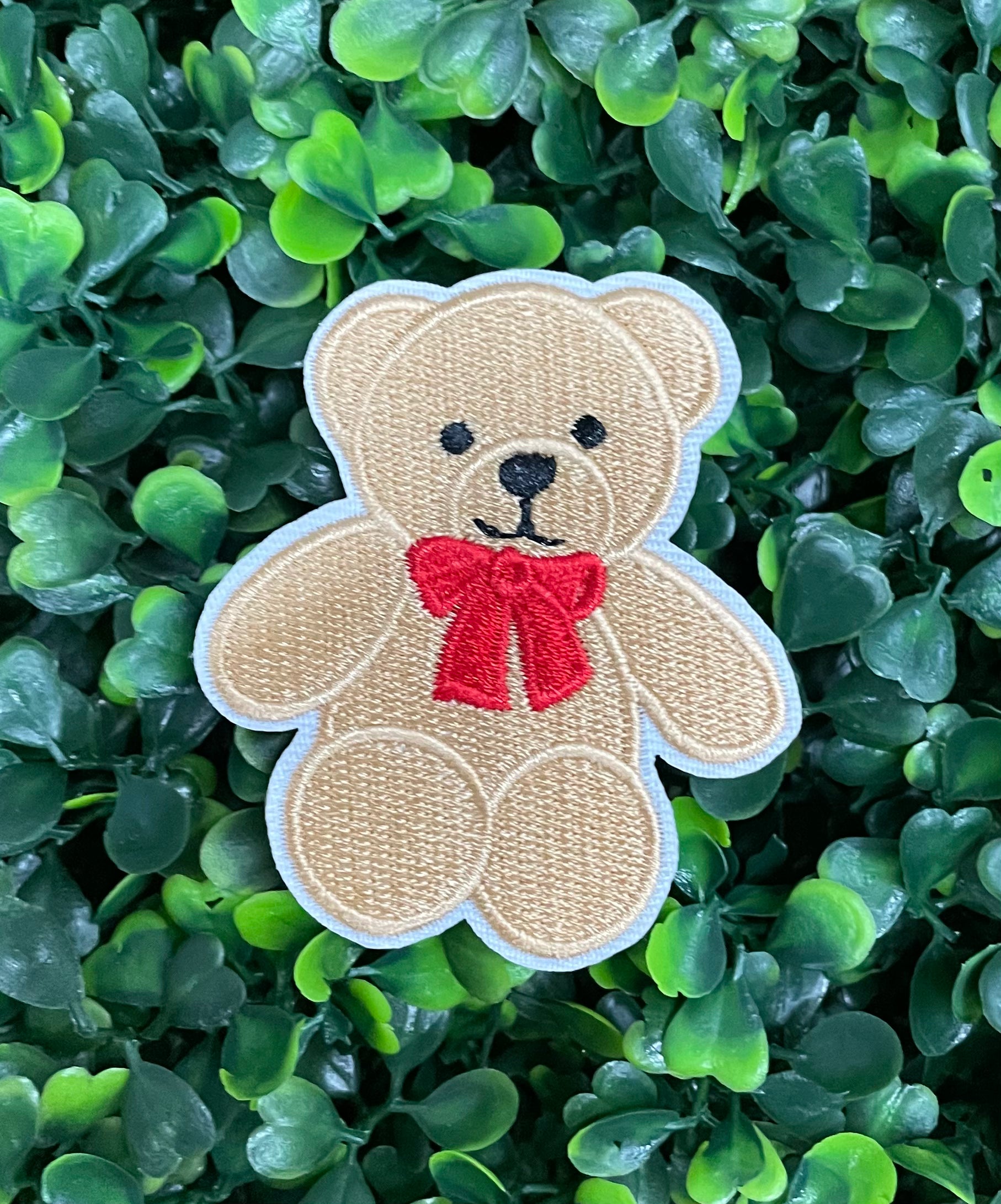 Embroidered Teddy Bear patch with a red bow set on a green backdrop