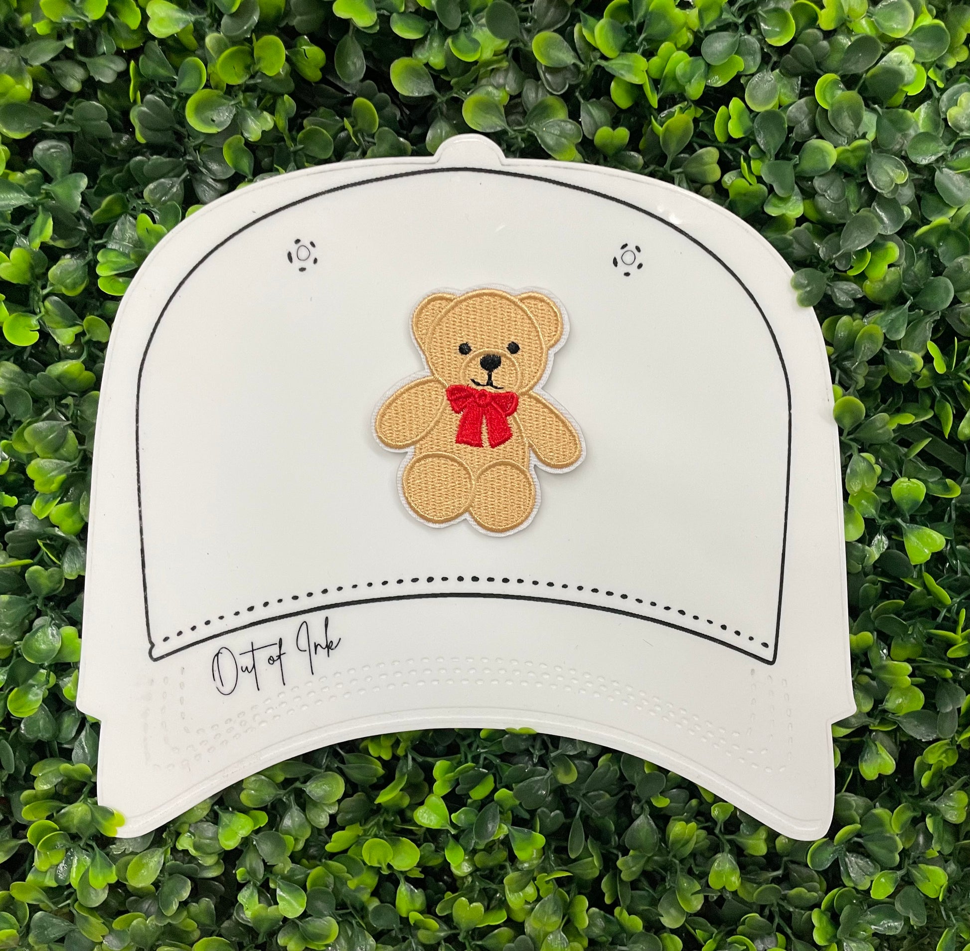 Embroidered Teddy Bear patch with a red bow set on a white hat