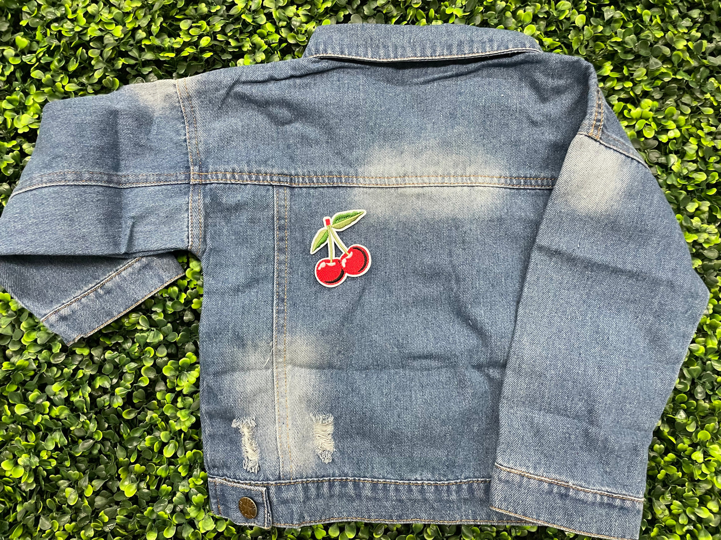 A patch with two red cherries and a green leaf embroidered on it, placed on a jean jacket
