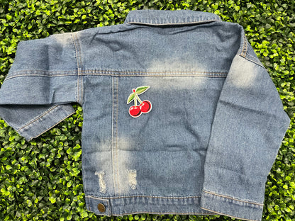 A patch with two red cherries and a green leaf embroidered on it, placed on a jean jacket