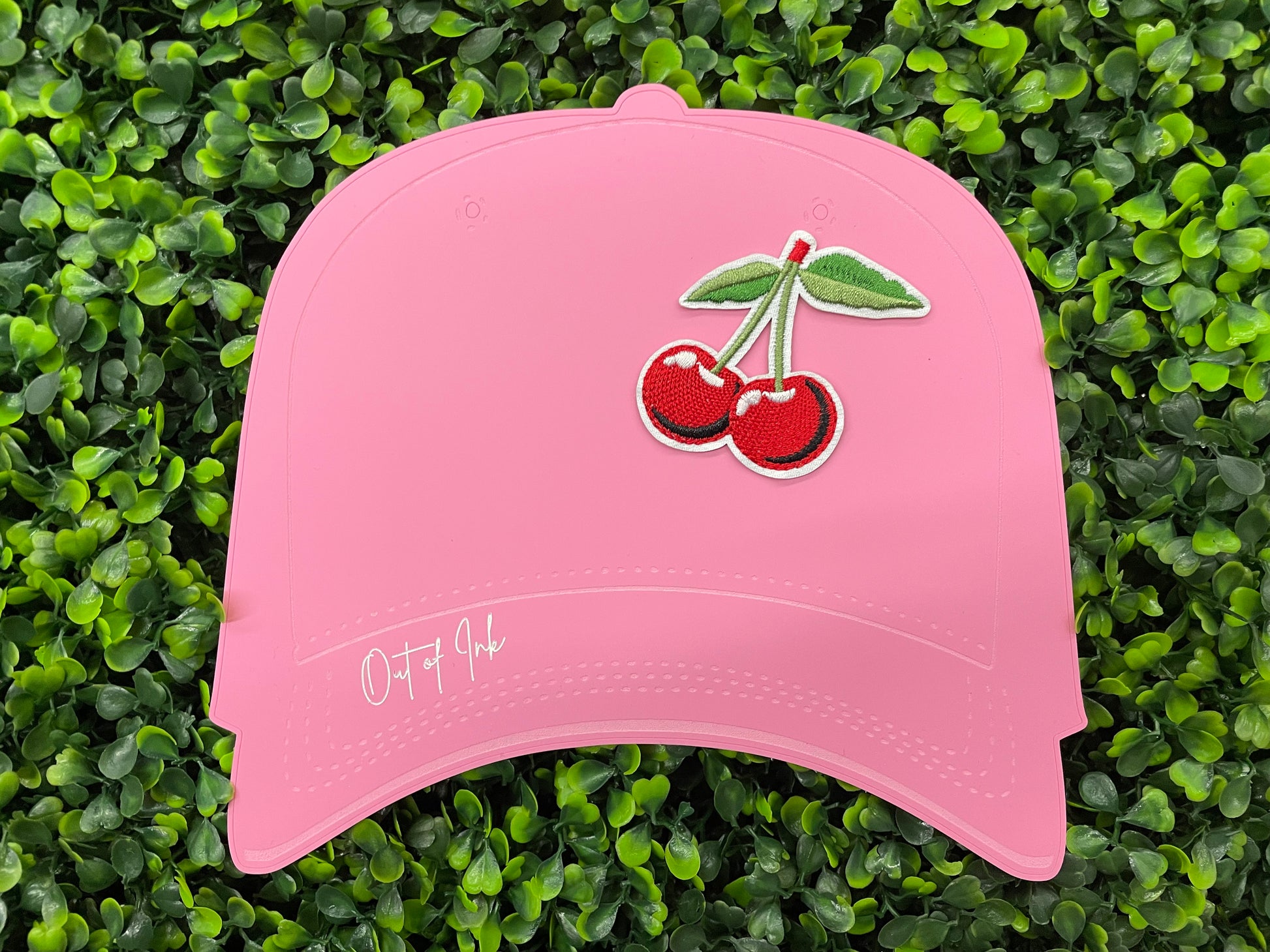 A patch with two red cherries and a green leaf embroidered on it, placed on a pink hat