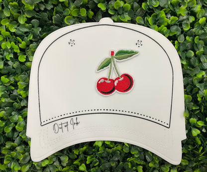 A patch with two red cherries and a green leaf embroidered on it, placed on a white hat graphic