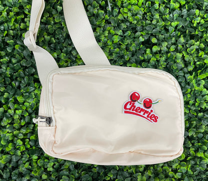An iron-on patch with an embroidered design of two cherries and the word 'Cherries' below them in red and green colors, placed on a white shoulder bag